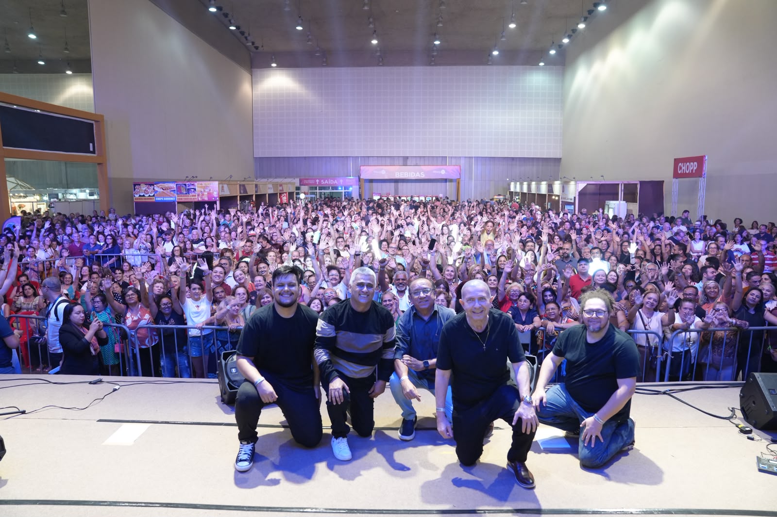 Os cinco integrantes da Banda Zona Proibida ajoelhados no palco, à frente da plateia em um show
